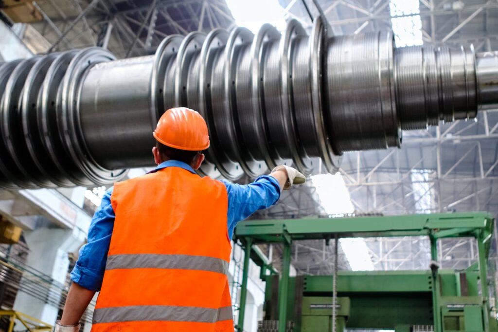 Worker in orange vest and hard hat with reaching up to a large metal pipeline