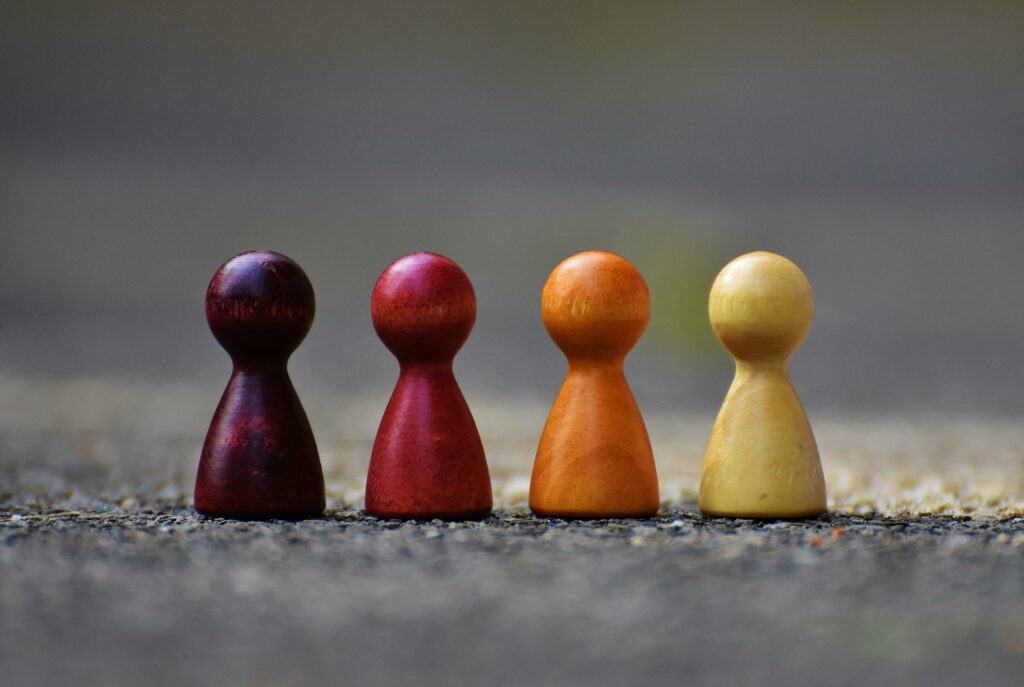 Four wooded colored toy pieces shaped like people sitting on ground