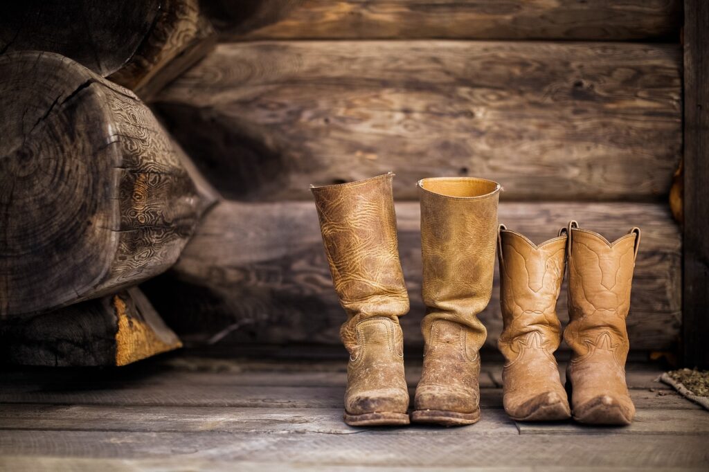 Two pairs of brown cowboy boots sitting on brown wooden porch